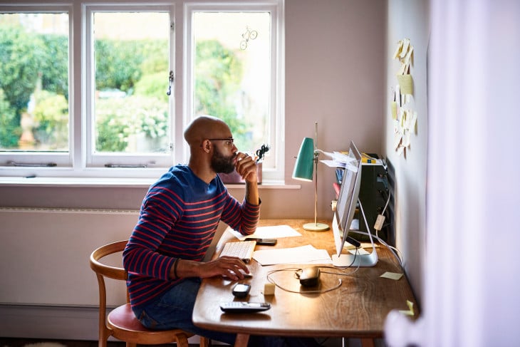 Man Sitting in Chair at Desk Working From Home on Computer