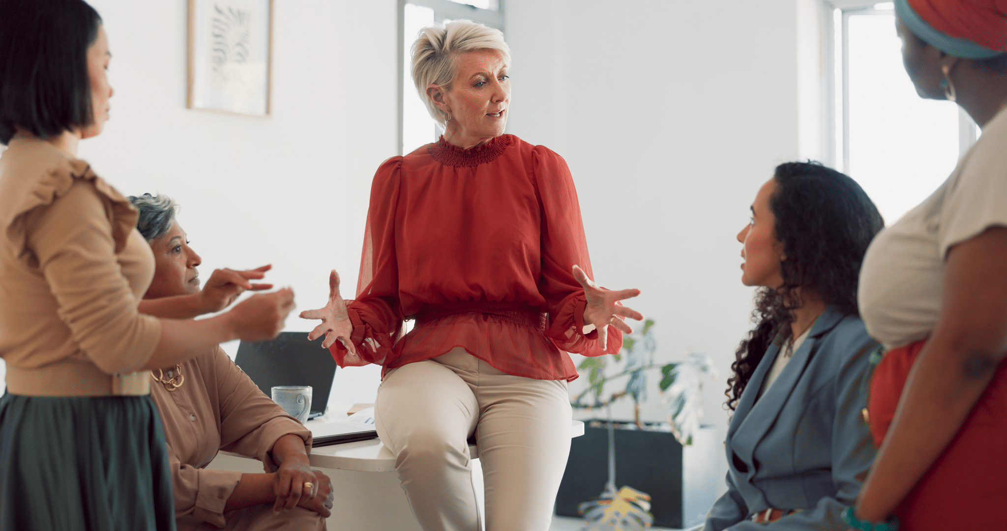 teamwork senior women sitting on desk in office talking to coworkers